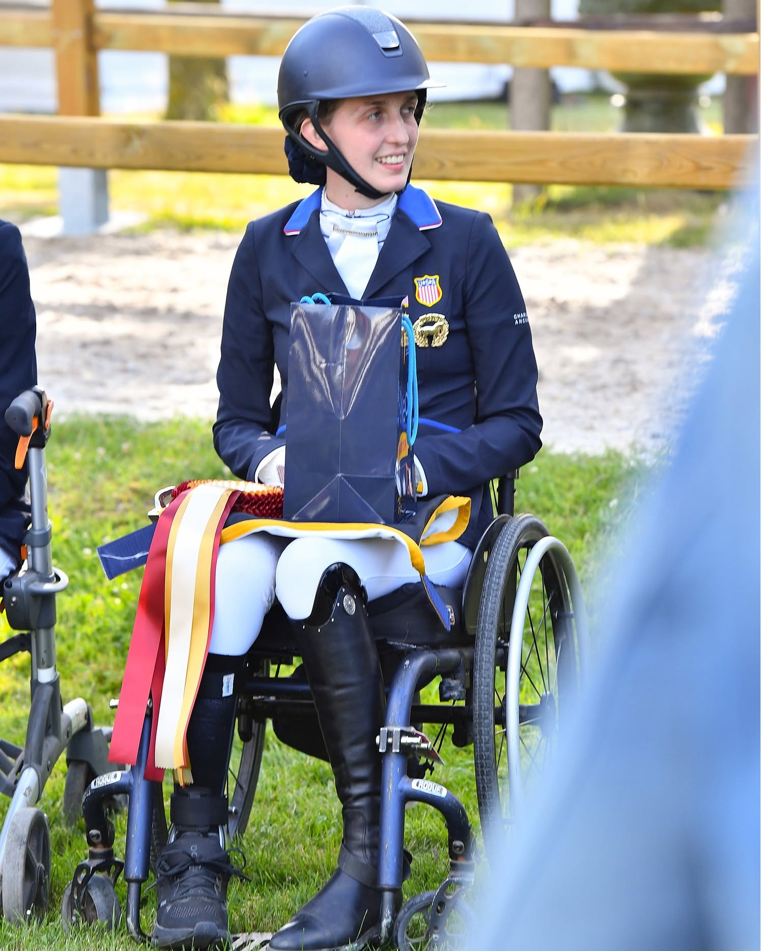 Fiona Howard smiling in her wheelchair holding championship ribbons after competing at the FEI Para Dressage World Championships